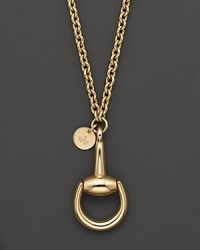 A bold horsebit pendant and a logo tag dangle from a gleaming 18K yellow gold chain. A bold horsebit pendant and a logo tag dangle from a gleaming 18K yellow gold chain.